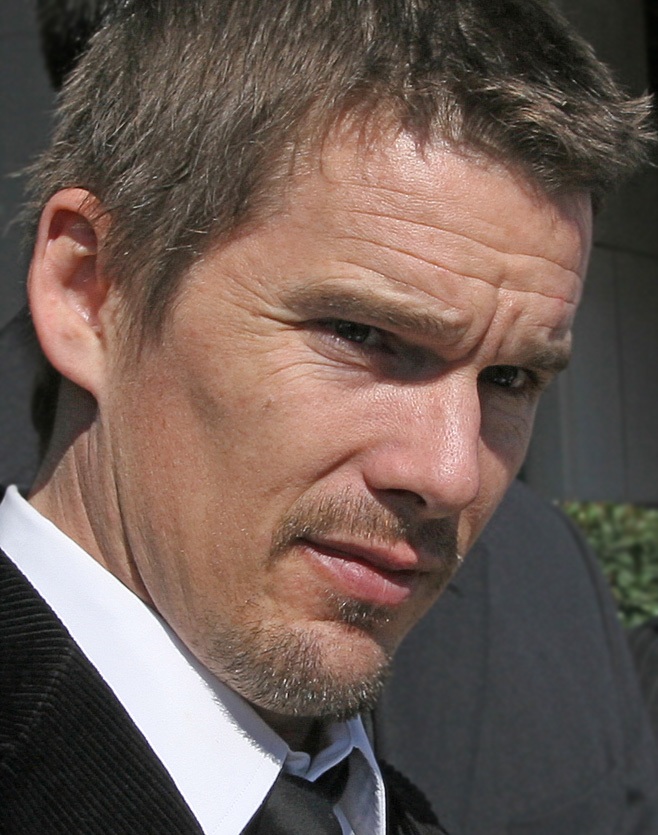 A closeup photo of a Caucasian male with light brown hair. The collar of a white shirt is visible in the photo, with a black jacket and black tie.