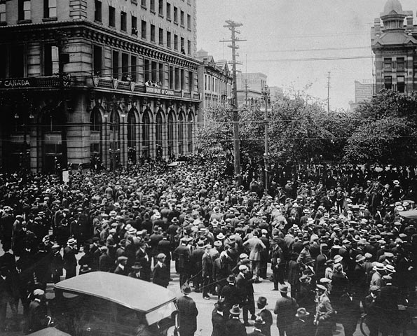 Large group of people in the middle of a city street beside a large concrete building