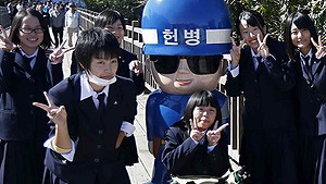 Japanese students pose for a photo with a statue of a South Korean military policeman