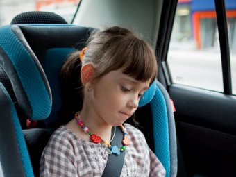 A young girl sitting in the back seat of a car in a car seat.