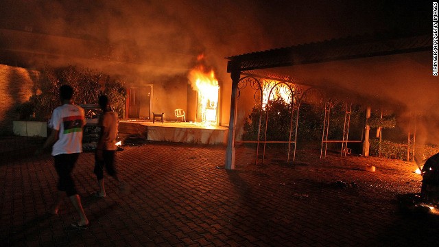 Onlookers walk past a burning truck and building in the compound on September 11.