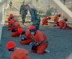  Detainees in orange jumpsuits sit in a holding area under the watchful eyes of Military Police at Camp X-Ray at Naval Base Guantanamo Bay, Cuba, during in-processing to the temporary detention facility on Jan. 11, 2002. The detainees will be given a basi