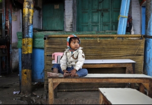 A boy sits on a bench in front of closed shops along a street in the old quarters of Delhi...