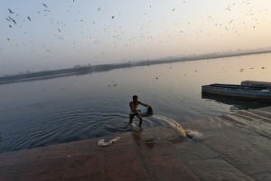 A man pours water using a bucket to clean the banks of river Yamuna during early morning in old...