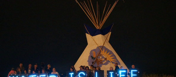 The Holders of the Light held several Idle No More water-related messages in front of the 2013 Indian Summer Festival’s tipi, prominently located on the State Park Island in front of the Indian Summer grounds. (Photo: Light Brigading / Flickr)