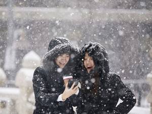 Women smile as they look at a picture on a mobile phone during snowfall in winter in central Seoul