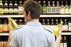 Young man in supermarket comparing bottles of oil.