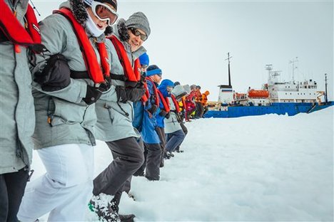 In this Tuesday, Dec. 31, 2013 image provided by Australasian Antarctic Expedition/Footloose Fotography, passengers from the Russian ship MV Akademik Shokalskiy link arms and stamp out a helicopter landing site on the ice near the trapped ship 1,500 nautical miles south of Hobart, Australia. Passengers on board a research ship that has been trapped in Antarctic ice for a week are expected to be rescued by helicopter, after three icebreakers failed to reach the paralyzed vessel, officials said Tuesday.