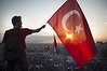 A protestor waves the Turkish flag from a roof top.