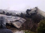 A man watches rescue workers working at the wreckage of Algerian military transport aircraft after it slammed into a mountain in the country’s rugged eastern region, Tuesday, Feb. 11, 2014.