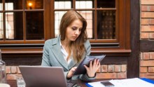 A woman sitting at a cafe working with a laptop, mobile table device and a mobile phone.