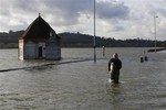 A man wades through a flooded road at Runnymede, England, Thursday, Feb. 13, 2014.