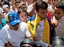 Draped in a Venezuelan national flag, opposition leader Leopoldo Lopez, second from right, is surrounded by anti-government demonstrators and media, just before Lopez surrenders to national guards, in Caracas, Venezuela, Tuesday, Feb 18, 2014. Lopez re-emerged from days of hiding to address an anti-government demonstration and then surrendered to authorities Tuesday in a move that he said will open the world's eyes to the increasingly authoritarian bent of Venezuela's socialist government.