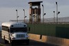 File - A Soldier assigned to the 115th Military Police Company of the Rhode Island Army National Guard stands watch in a guard tower at Camp Delta, Joint Task Force Guantanamo as a Navy shuttle bus passes by.