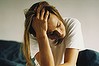 young woman sitting on bed with head in hand