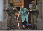 A woman sweeps away the broken glass as two unidentified armed men guard the entrance to the local government building in downtown Simferopol, Ukraine, on Sunday, March 2, 2014.