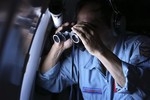 Vietnamese Air Force Col. Pham Minh Tuan uses binoculars on board a flying aircraft during a mission to search for the missing Malaysia Airlines flight MH370 in the Gulf of Thailand over the location where Chinese satellite images showed possible debris from the missing Malaysian jetliner, Thursday, March 13, 2014.