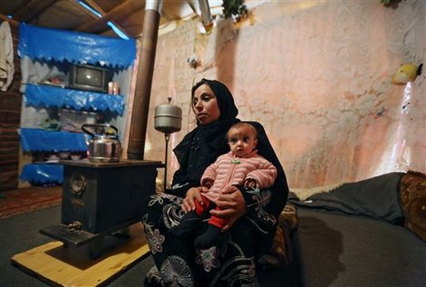 In this Tuesday, March 11, 2014 photo, Mervat, 31, speaks during an interview with The Associated Press as she holds her 9-month-old daughter Shurouk inside their tent at a camp for Syrian refugees in Kab Elias, in Lebanon's Bekaa Valley. Trapped in her northern Syrian village by fighting, Mervat watched her newborn baby progressively shrink.