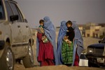 Afghan refugee women wearing burqa as they carry their children, as they walk next to a refugee camp on the outskirts of Islamabad, Pakistan