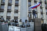 Pro-Russian masked activist waves a Russian national flag above Ukrainian police at the regional administration building in Donetsk, Ukraine, Sunday, April 6, 2014.