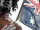 An Aboriginal performer stands in front of an Australian flag