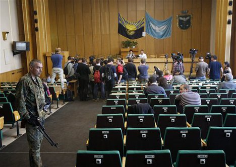 An armed pro-Russian man stands guard at the back of a room during press conference of Vacheslav Ponomarev, the self-proclaimed mayor of Slovyansk and Lidia Bartasevic, president of Slovyansk's election commission in Slovyansk, eastern Ukraine, Monday, May 12, 2014.