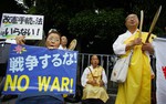 A woman holds an anti-war placard and a sign as Buddhist monks beat drums and chant sutras during a rally against Japan's plan to reform constitution in Tokyo Thursday, May 15, 2014.