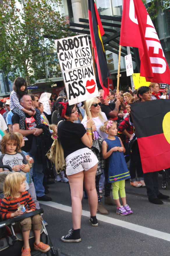 Woman in shorts and placard with caption ' Abbott can kiss my perky lesbian ass'