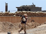 A Kurdish peshmerga fighter carries his weapon walks onto his base, where two flags of the Islamic State in Iraq and the Levant (ISIL) are seen on a building, right, and water tower, left, at the front line with the al-Qaida-inspired militants in Tuz Khormato, 100 kilometers (62 miles) south of the oil rich province of Kirkuk, northern Iraq, Wednesday, June 25, 2014.