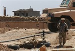 A Kurdish peshmerga fighter carries his weapon on his base, near where two flags of the Islamic State in Iraq and the Levant (ISIL) are seen on a building, right, and water tower, left, at the front line with the al-Qaida-inspired militants in Tuz Khormato, 100 kilometers (62 miles) south of the oil rich province of Kirkuk, northern Iraq, Wednesday, June 25, 2014.