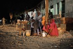 File - Somali women sell tea on the side of the road in Baidoa, while Ethiopian soldiers as part of the African Union Mission in Somalia, conduct a night patrol through the city on June 22, 2014.