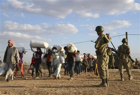 Turkish soldiers stand guard as Syrian refugees gather at the border in Suruc, Turkey, late Saturday, Sept. 20, 2014.