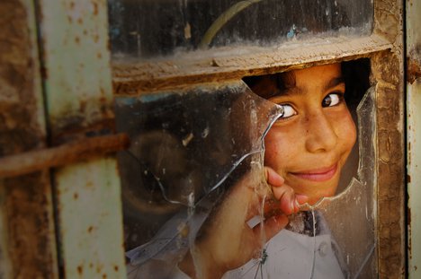 File - An Iraqi girl peeks out out the broken classroom window to watch U.S. Army Soldiers from Bravo Company, 2nd Battalion, 22nd Infantry Regiment, 10th Mountain Division, deliver much needed desks for the school in Nawaful village, Kirkuk Province, Iraq, March 25, 2008.