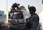 An Iraqi federal policeman stands guard as his colleague searches a car at a checkpoint in Baghdad, Iraq, Saturday, Oct. 11, 2014.