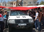 In this photo released by the Syrian official news agency SANA, a UN observers vehicle passes under a huge Syrian flag held by Syrian President Bashar Assad supporters during their visit to the pro-Syrian regime neighborhoods, in Homs province, central Syria, on Monday April 23, 2012.