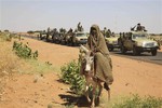 File - In this Thursday, Nov. 20, 2014 photo taken on a government organized media tour, a woman rides a donkey past a convoy of government troops in Tabit village in the North Darfur region of Sudan, where allegations surfaced of rape of women by government allied troops.