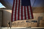 A U.S. Army soldier with the 25th Infantry Division, 3rd Brigade Combat Team, 2nd Battalion 27th Infantry Regiment based in Schofield Barracks, Hawaii, walks past an American Flag hanging in preparation for a ceremony commemorating the tenth anniversary of the 9/11 attacks, Sept. 11, 2011 at Forward Operating Base Bostick in Kunar province, Afghanistan.