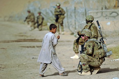 File - Alaskan National Guard Sgt. Brain Reid talks with a local Afghan child during a dismounted patrol to a Department of Public Works facility Aug. 8, 2012, in Kandahar, Afghanistan.