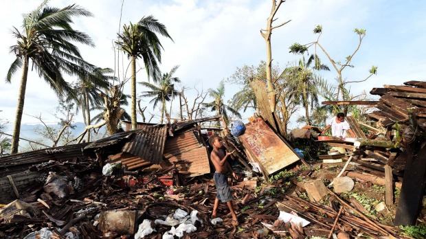 A boy plays with a ball as his mother searches through the ruins of their family home in Port Vila, Vanuatu. 