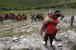 A local Nepalese person waits as he carries an injured victim of the recent earthquake to be evacuated by an Indian Air Force helicopter at Chhintang Phedi village, in Nepal, Wednesday, April 29, 2015.