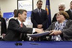 Gov. Sam Brownback, left, shakes hands with Department for Children and Families secretary Phyllis Gilmore, right, after signing a welfare reform bill into law in Topeka, Kan., Thursday, April 16, 2015.