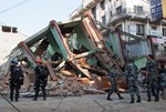 Rescue workers stand beside a building that collapsed in an earthquake in Kathmandu, Nepal, Tuesday, May 12, 2015.