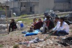 File - In this picture taken on Saturday April 18, 2015, a Kurdish displaced family sit in the open air field near their house which was destroyed during the battle between the U.S. backed Kurdish forces and the Islamic State fighters, in Kobani, north Syria.