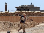 In this June 25, 2014, file photo, a Kurdish peshmerga fighter carries his weapon walks onto his base, where two flags of the Islamic State in Iraq and the Levant (ISIL) are seen on a building, right, and water tower, left, at the front line with the al-Qaida-inspired militants in Tuz Khormato, 100 kilometers (62 miles) south of the oil rich province of Kirkuk, northern Iraq.