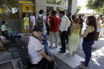 People stand in a queue to use an ATM of a bank as others sit on chairs put out from the branch in Athens, Tuesday, July 7, 2015. Greek Prime Minister Alexis Tsipras was heading Tuesday to Brussels for an emergency meeting of eurozone leaders.