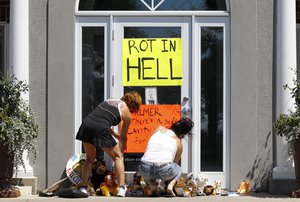 Women place a sign outside Dr. Walter James Palmer's dental office in Bloomington, Minn., Wednesday, July 29, 2015. Palmer reportedly paid $50,000 to track and kill Cecil, a black-maned lion, just outside Hwange National Park in Zimbabwe. (AP Photo/Ann Heisenfelt)