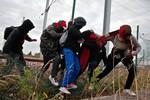 Migrants step over a fence as they escape from railway police officers, in Calais, northern France, Wednesday, July 29, 2015.