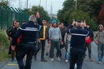 Police officers block migrants along a road to prevent their access to train tracks which lead to the Channel Tunnel, in Calais, northern France, Wednesday, July 29, 2015.