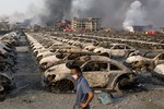 In this photo taken Thursday, Aug. 13, 2015, a man walks past the charred remains of new cars at a parking lot near the site of an explosion at a warehouse in northeastern China's Tianjin municipality.