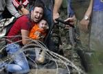 A migrant man holding a boy reacts as they are stuck between Macedonian riot police officers and migrants during a clash near the border train station of Idomeni, northern Greece, as they wait to be allowed by the Macedonian police to cross the border from Greece to Macedonia, Friday, Aug. 21, 2015.